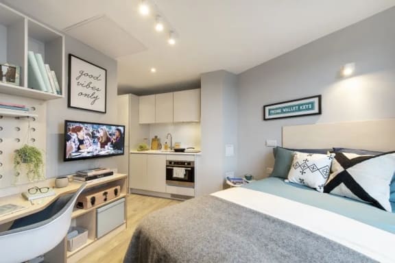 a bedroom with a bed and a desk and a kitchen