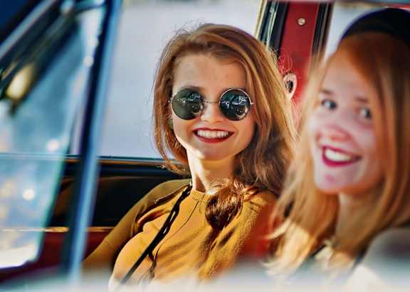 Two women are sitting in a car, one is wearing sunglasses.