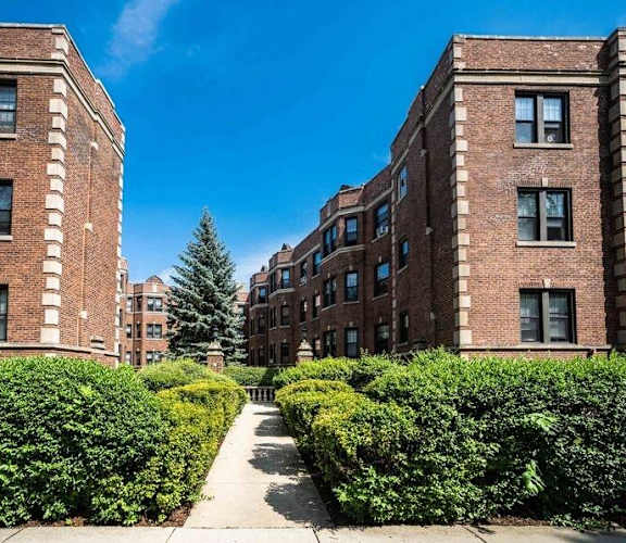 A pathway leads between two rows of hedges in front of a brick building.
