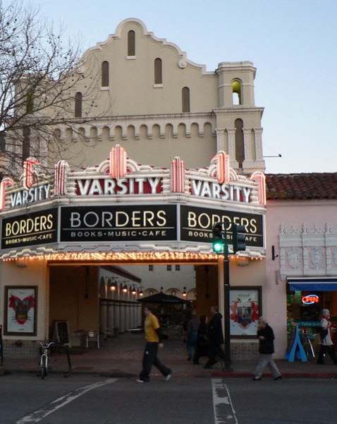 a theater on the corner of a street with people walking