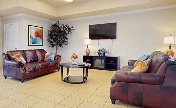 A living room with a brown leather couch, a black table, and a television mounted on the wall.