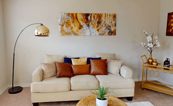 A living room with a white couch, a lamp, a plant, and a painting on the wall.