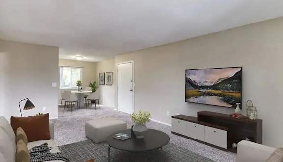 A living room with a grey carpet and a painting on the wall.