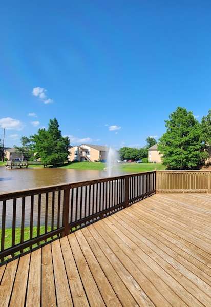 A wooden deck overlooks a body of water with a house and trees in the background.