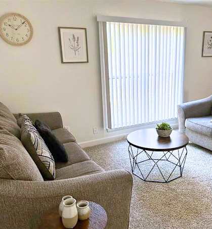 A living room with a grey couch, a coffee table, and a clock on the wall.