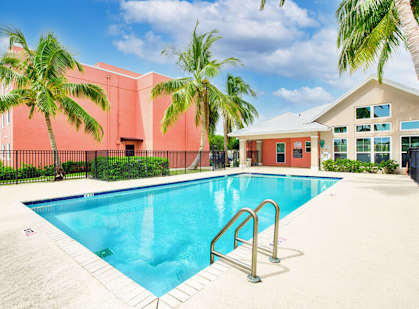 A swimming pool surrounded by palm trees and a red building.