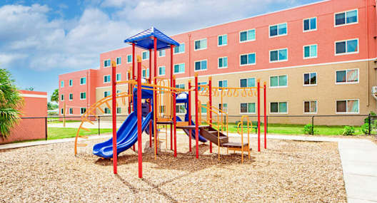 A playground with a blue slide and a red and yellow structure in front of a red building.