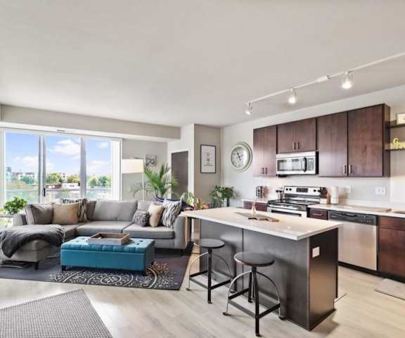 A living room and a kitchen with a plush couch, footrest, doors to a balcony, and stainless-steel appliances in the kitchen at Blue and Lime Apartments. 