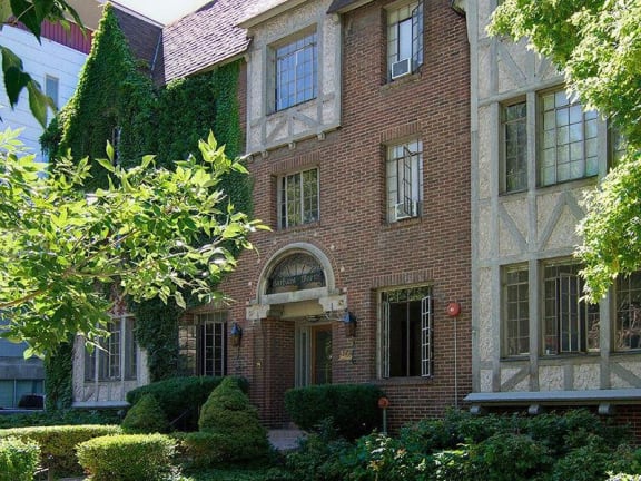 a brick house with a tree and bushes in front of it