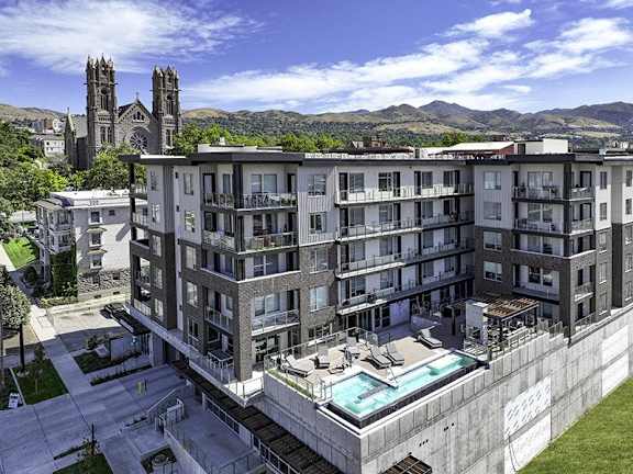 A large apartment complex with a pool and a view of a church and mountains in the background.
