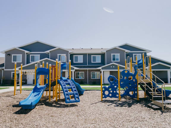 A playground with a blue slide and a yellow and blue climbing frame in front of a building.