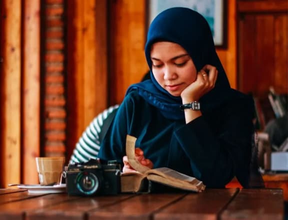 a young woman sitting at a table reading a book