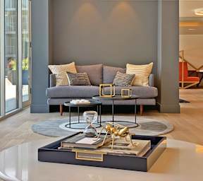 A modern living room with a grey couch, a coffee table with a glass top, and a book with a golden bookend.