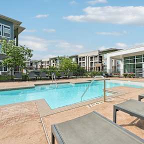 A swimming pool surrounded by a brick patio and lounge chairs.