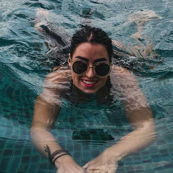 A woman with sunglasses is swimming in a pool.