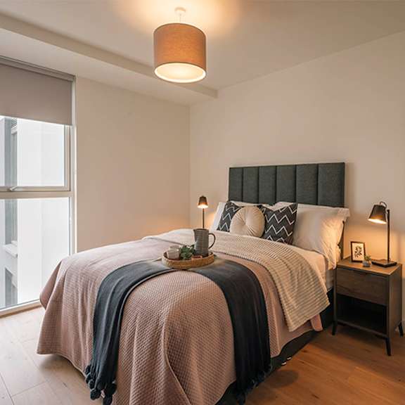 A bed with a pink blanket and pillows is in a room with a lamp on a side table at Cherrywood Apartments, D18 VY3V, DUBLIN 18