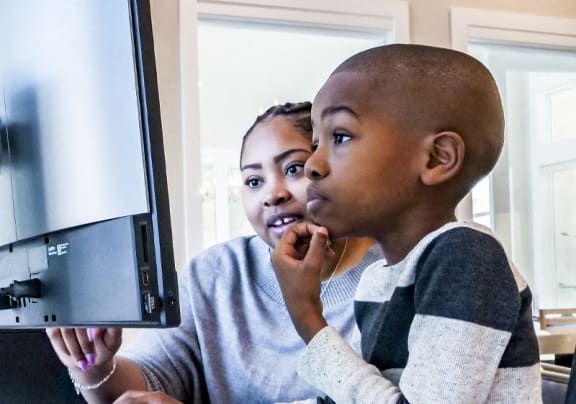 a boy and a woman looking at a computer monitor