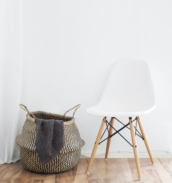 Basket sitting next to a chair in front of a white wall