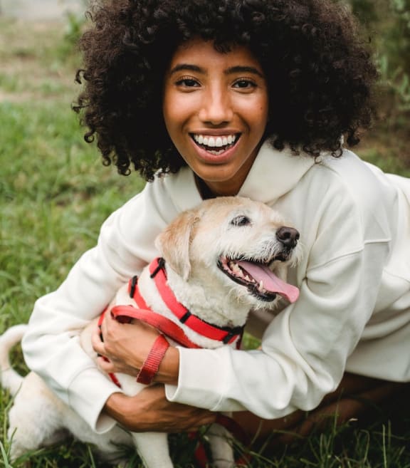 a smiling African-American woman with a white dog in a red and white harness