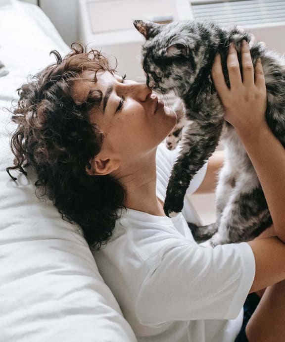 a woman laying in bed with a cat on her face