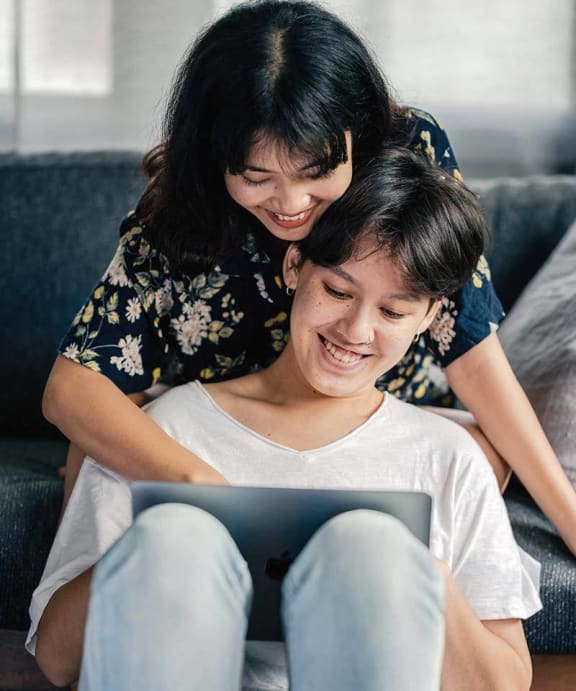 a woman and a girl sitting on a couch looking at a tablet