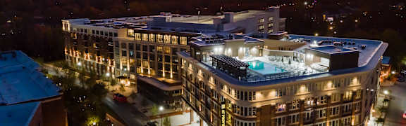 A large, modern building with a pool in the middle is surrounded by trees and lights.