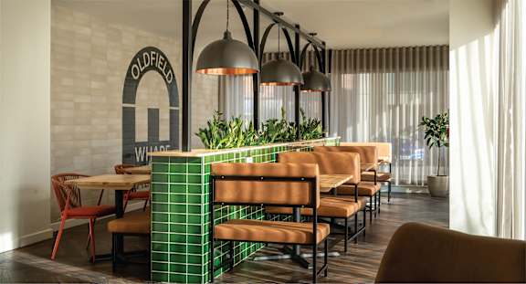 A restaurant with a green tiled wall and wooden chairs.
