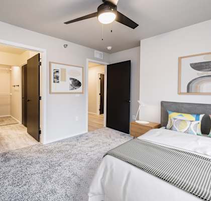 A bedroom with a bed, a ceiling fan, and a painting on the wall.