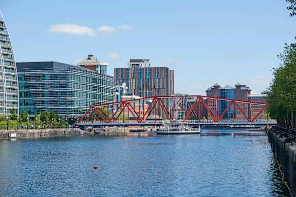 A red bridge spans a calm body of water with buildings in the background.