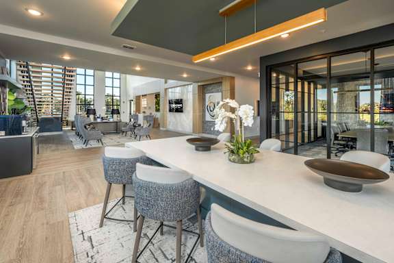 A modern kitchen with a long white island and grey chairs.