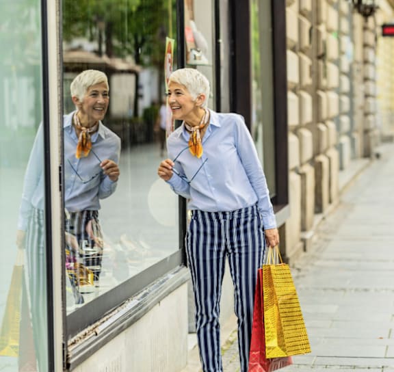 A woman with a yellow and red shopping bag is standing on a sidewalk.