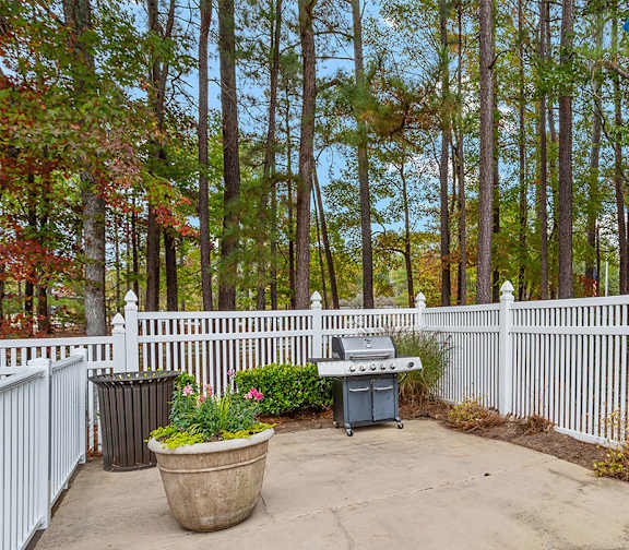 A backyard with a white fence and a grill.