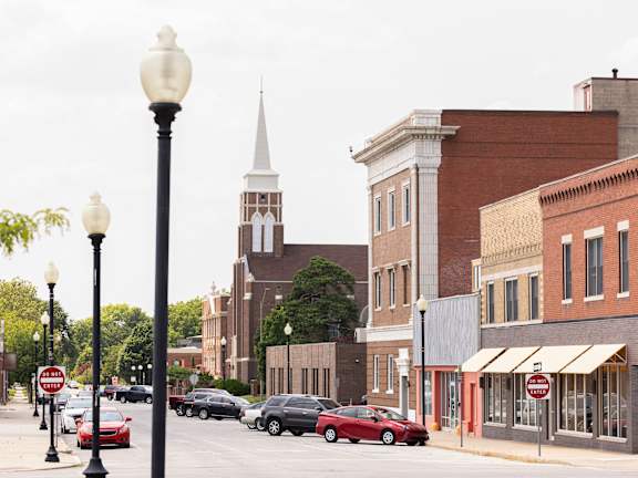 A street view of a town with a church spire in the background.