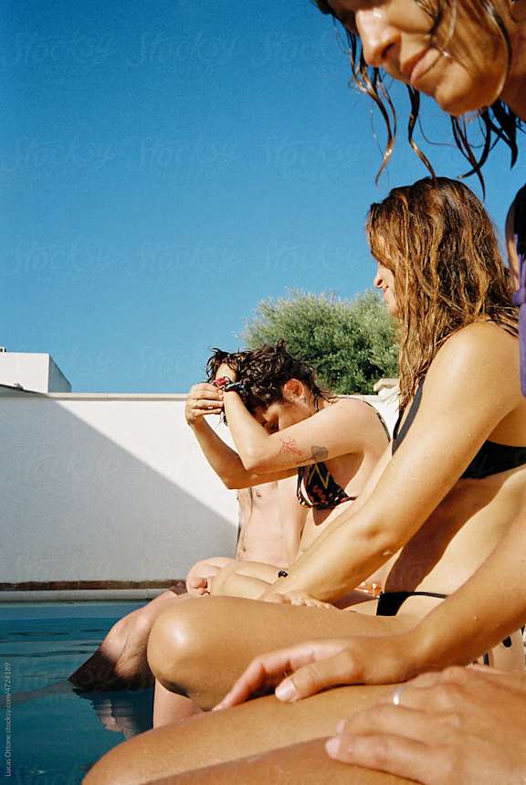 a group of women in bathing suits sitting around a swimming pool