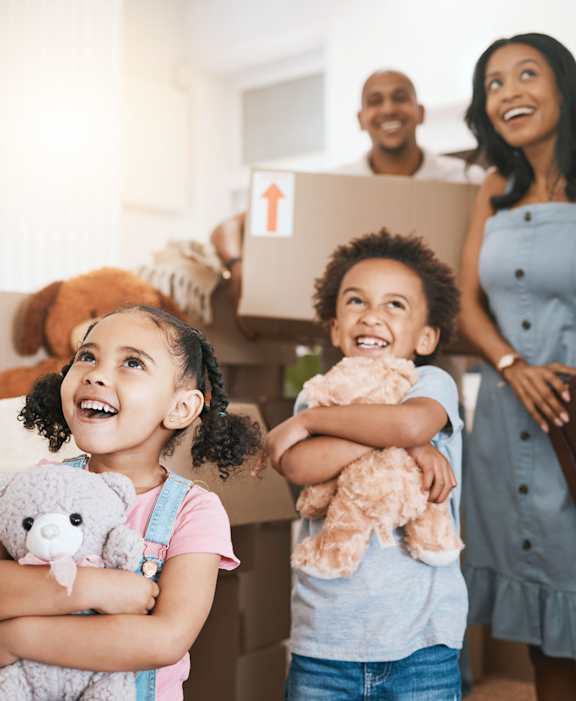 A family of four is standing in a room with boxes, indicating they are moving in.