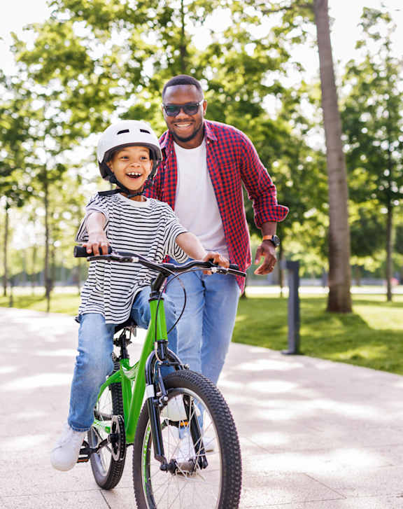 A man is teaching a child to ride a bike in a park.