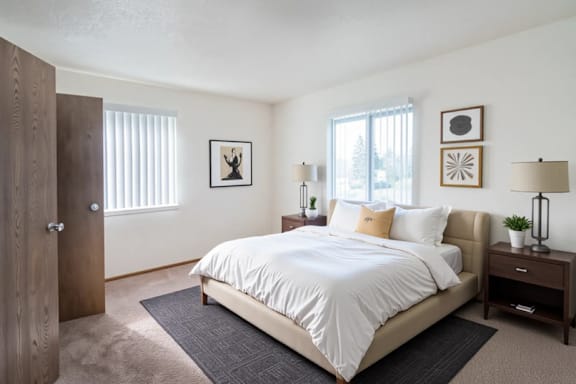 A bedroom with a large bed, a nightstand, and a window with blinds.