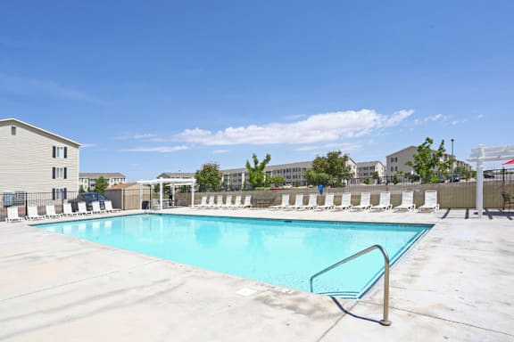 A swimming pool surrounded by a metal fence and lounge chairs.