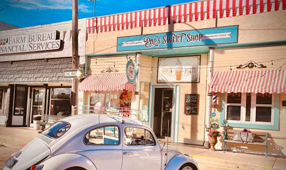A white Volkswagen Beetle is parked in front of a building with a red and white striped awning.