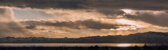 The sun is shining through the clouds over a mountain range.
