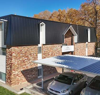 A modern building with a black roof and a parking area in front.