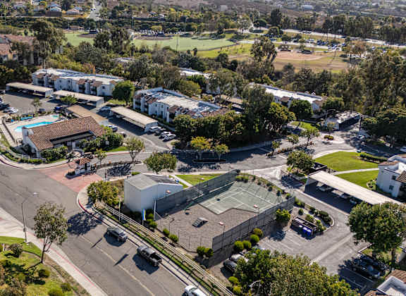 A large building with a green roof is surrounded by trees and a parking lot.