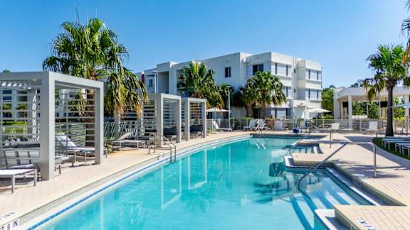 A large swimming pool in front of a white building with palm trees.at Icon One, Daytona Beach