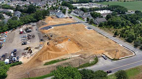 A construction site is surrounded by a parking lot and residential houses.