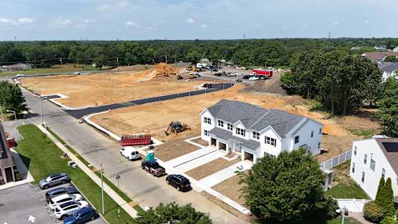 A construction site is surrounded by a parking lot and a few houses.