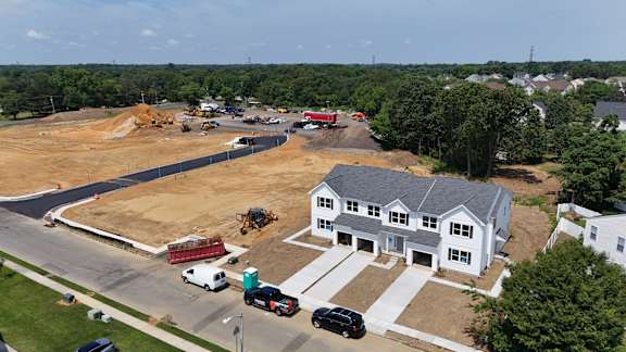 A construction site is seen from an aerial view with a white house in the background.