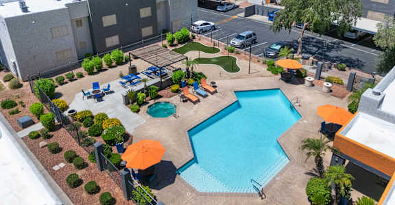A large swimming pool surrounded by a patio area with chairs and umbrellas.