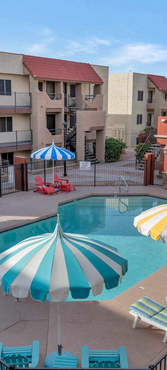 A pool surrounded by a fence and umbrellas in front of apartment buildings at Urban WalkApartments on 6th Avenue, Arizona 85016