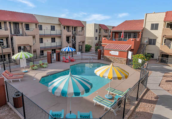 A pool surrounded by a fence and umbrellas in front of apartment buildings at Urban WalkApartments on 6th Avenue, Phoenix 85016