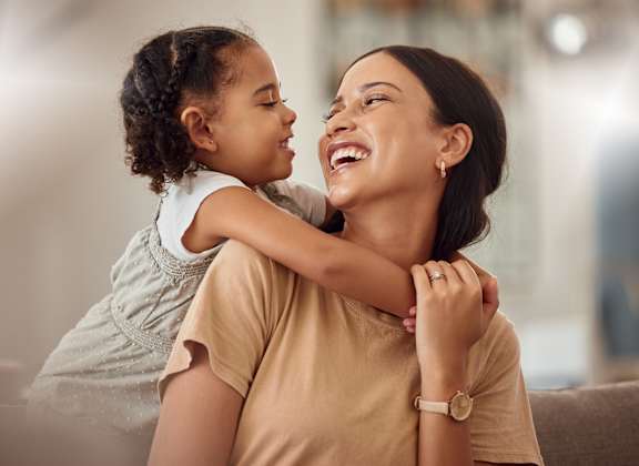 A woman is hugging a little girl from behind.